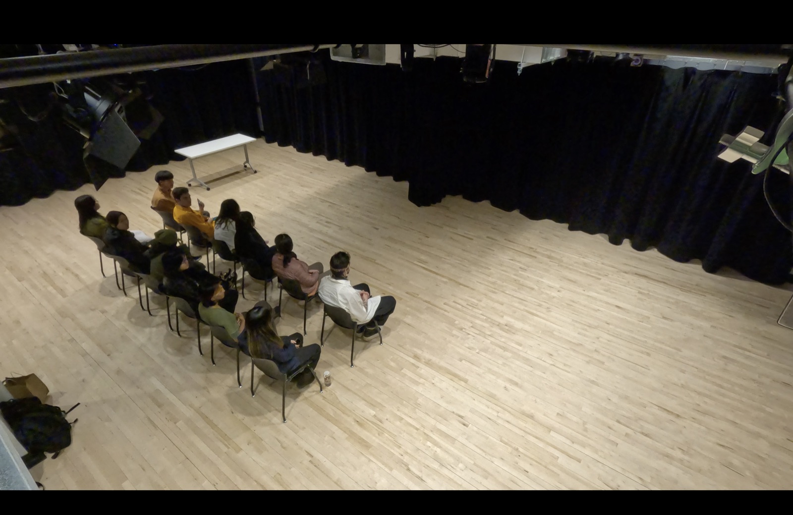 People sitting in different parts of the room: cross-legged in various places, some are sitting on chairs, one is lying down.